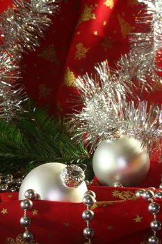two silver Christmas balls and tinsel chain lie on red fabric