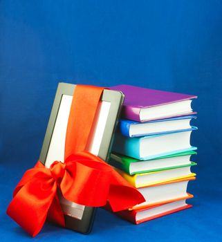 Electronic book reader tied up with red ribbon with stack of books