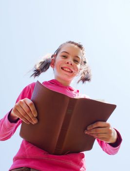 Teen girl reading the Bible against blue sky