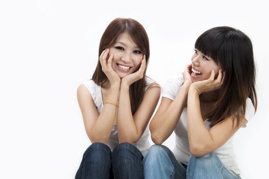 Two happy young women sitting on white background