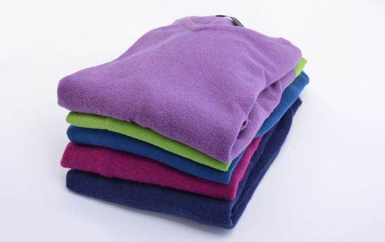 Pile of colorful, folded cashmere or merino wool jumpers isolated on white