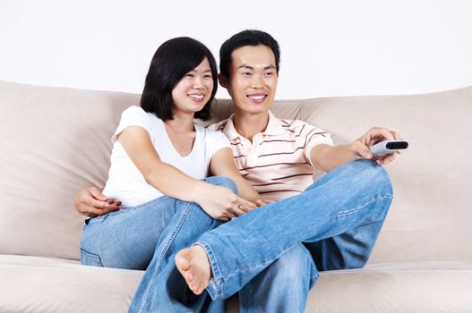 Asian couple sitting on sofa watching TV together.