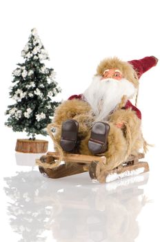 Miniature of Santa Claus on sleigh and a pine tree with snow, on white reflective background.