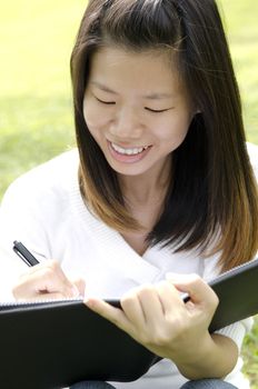 Asian student sitting at outdoors, studying and writing.