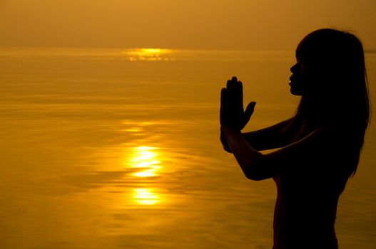 Woman with hands folded at seaside during sunset.