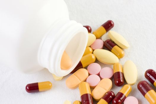 Pills spilled out of a bottle and scattered on white background. 
