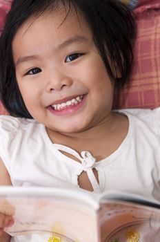 Little Asian girl lying on bed and reading 