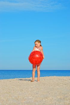 Happy little girl with red ball on the beach