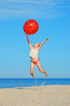 Jumping little girl with red ball on the beach