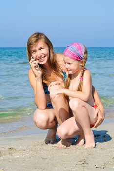 Mother and daughter talking cellular phone on the beach