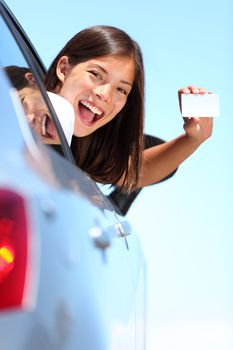 Young woman in car showing blank drivers license or sign out the car window. Happy lovely mixed race Asian Caucasian female model outside.