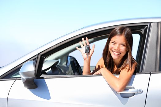 Asian car driver woman smiling showing new car keys and car. Mixed-race Asian and Caucasian girl.