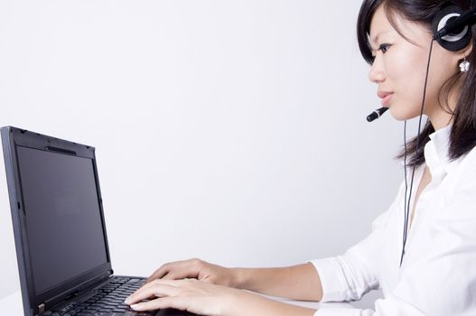 Asian consultants with headsets working on laptop computer on grey background. 