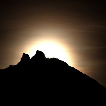 Moon shining bright behind black mountains