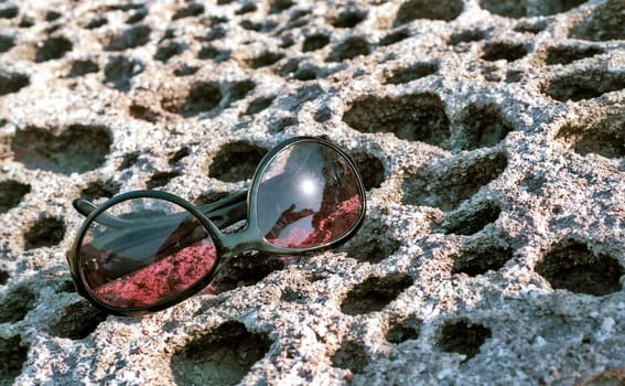 Sun glasses on honeycomb stone with reflection of Sun and a hand