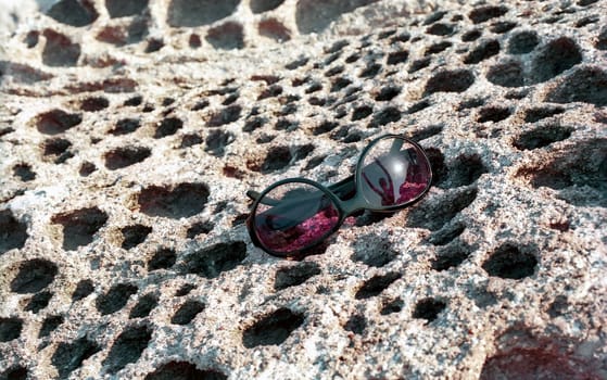 Sun glasses with reflection of Sun and girl on the honeycomb stone surface 