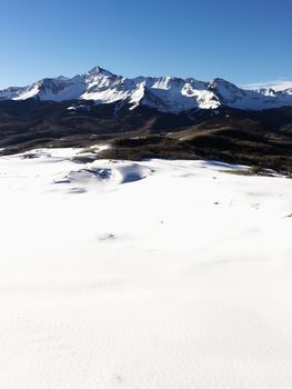 Aerial landscape of Colorado Rockies with snow covered valley in foreground.