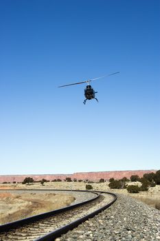 Low angle shot of helicopter flying over train tracks.