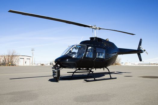 Black helicopter with camera mounted on front parked at airport tarmac.