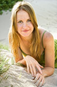Portrait of pretty redheaded woman lying in sand looking at viewer.