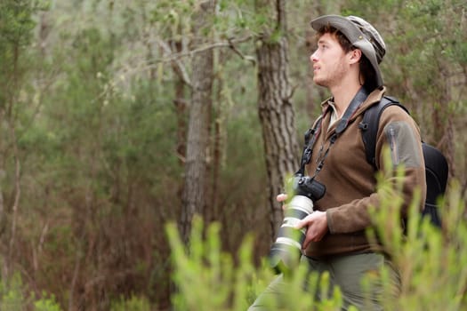 Photographer in nature taking pictures in forest. Outdoors man hiking with DSLR camera with tele lens looking to the side copy space. From Aguamansa, Tenerife, Spain