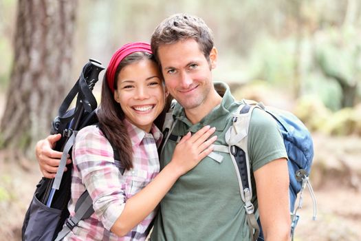 Happy young couple hiking smiling. Woman and man hikers looking at camera. Male hiker holding around woman hiker. Mixed race Asian Caucasian couple.
