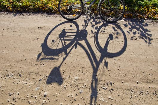 Standing bicycle and shadow of it on gravel road.