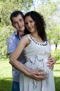 Man and a pregnant woman hugging in summer park