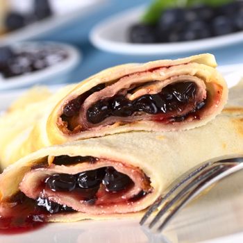 Pancakes filled with blueberry jam with fresh blueberries and jam in the back (Selective Focus, Focus on the front of the upper pancake roll)