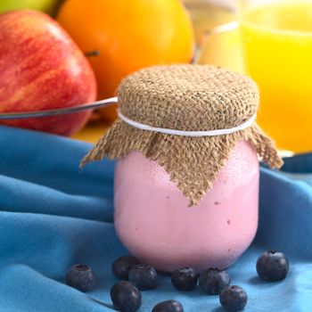 Blueberry yogurt in glass with fresh blueberries in front with fresh fruits and orange juice in the back (Selective Focus, Focus on the front part of the top of the yogurt) 