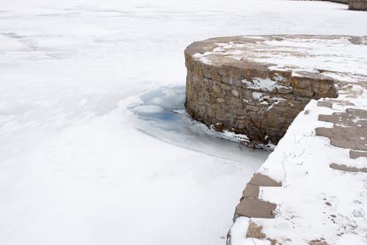 Old stone masonry pier on the frozen water reservoir 