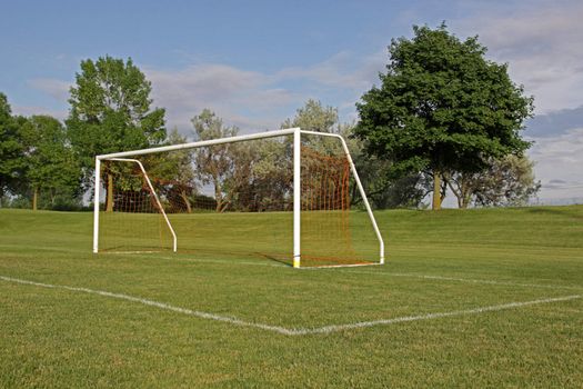 An empty soccer goal with trees in the background.
