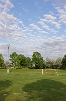 A mixed sky over an unoccupied soccer field with trees in the background.

