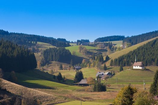 Farmland, farmhouses with chapel and forested hills in Black Forest, rural Germany.