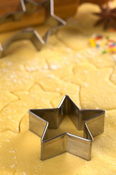 Star-shaped cookie cutter and other Christmas shapes cut into dough (Selective Focus, Focus on the two front edges of the star-shaped cutter)