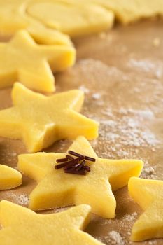 Unbaked star-shaped cookies with chocolate sprinkles on floured wooden surface (Selective Focus, Focus on the front of the chocolate sprinkles)