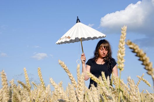 Young woman standing with little white umbrella in the field wheat.