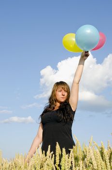 Young woman holding three different colored balloons in the field of wheat.