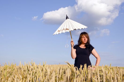 Young woman standing with little white umbrella in the field wheat.