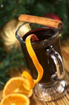 Hot spiced mulled wine garnished with orange peel and cinnamon stick (Selective Focus, Focus on the front rim of the glass and the orange peel at the rim)