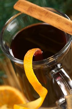 Hot spiced mulled wine garnished with orange peel and cinnamon stick (Selective Focus, Focus on the front rim of the glass and the orange peel at the rim)