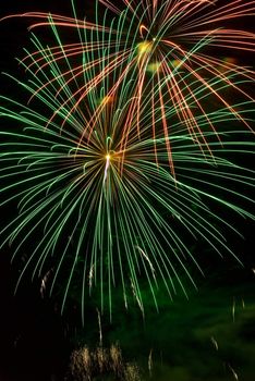 A green and orange burst of fireworks in the night sky.