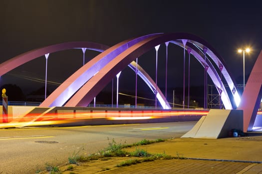 Pink steel girders of urban road bridge illuminated at night.