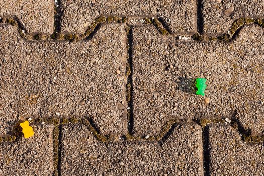 Two gummi baers laying separated on paved walkway.