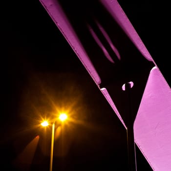 Detail of pink steel girder of urban road bridge illuminated at night.