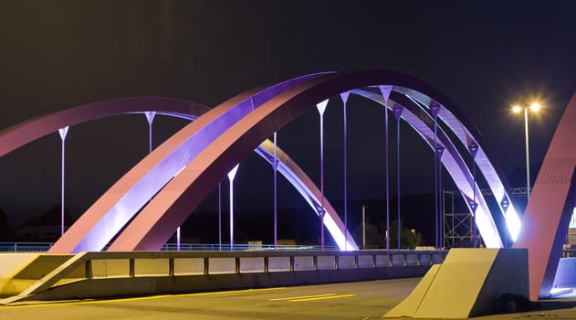 Pink steel girders of urban road bridge illuminated at night.