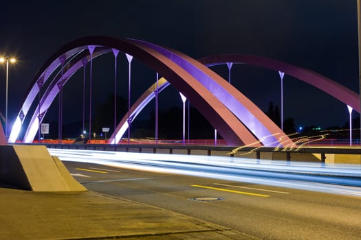 Pink steel girders of urban road bridge illuminated at night.