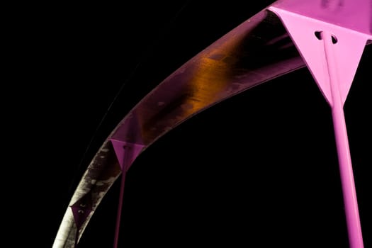 Detail of pink steel girder of urban road bridge illuminated at night.