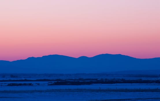 Snow covered fields and the distant Boulder Mountains after sunset in winter, north of Bozeman, Gallatin County, Montana, USA