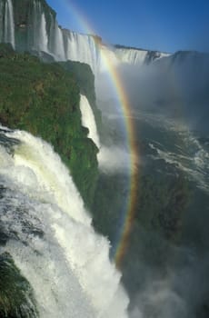 Large waterfalls with white water falling over cliff. Green vegitation and rainbow. Iguacu Falls, Brazil.